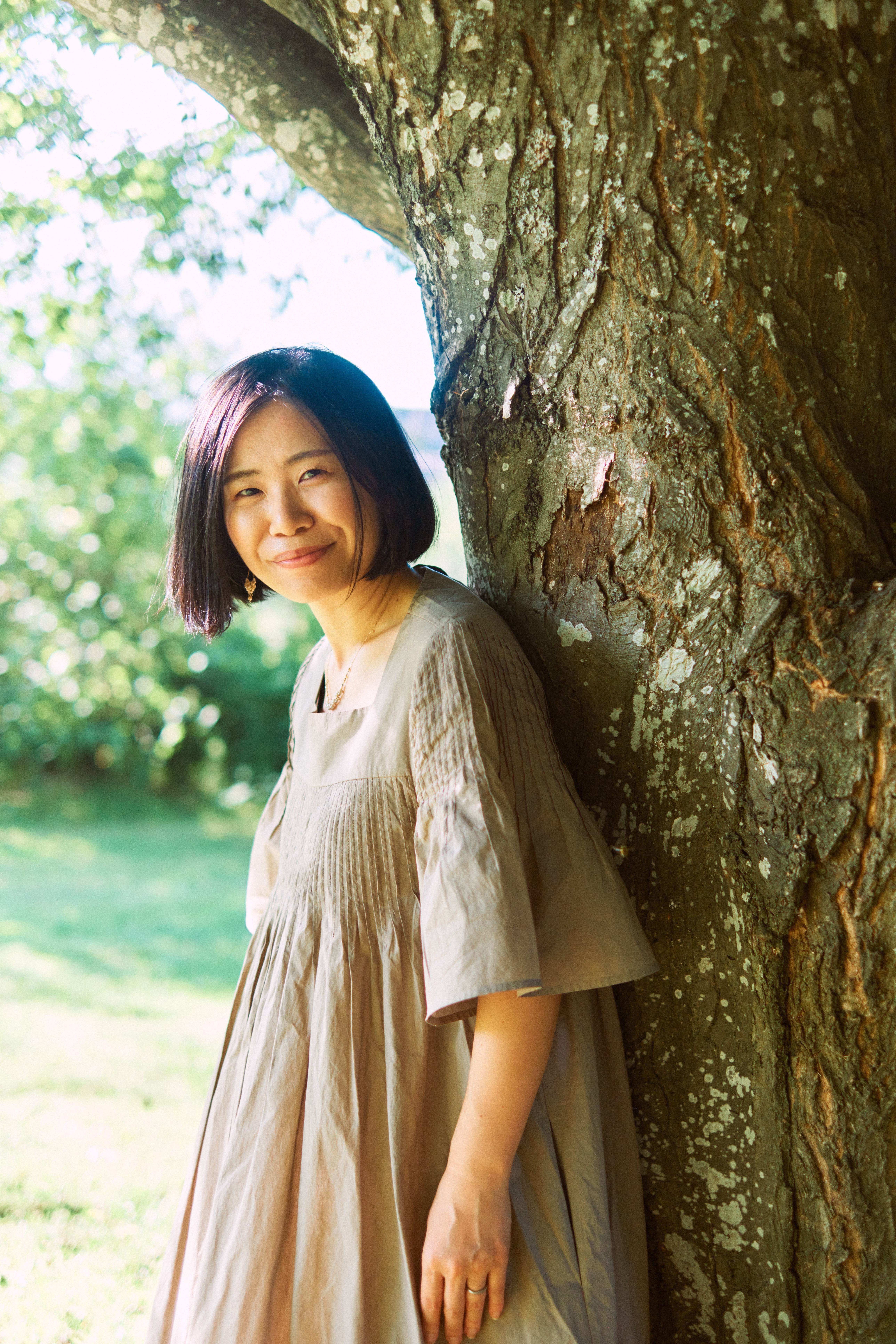 木に寄り添って微笑む、音声心理士 Rie のポートレート